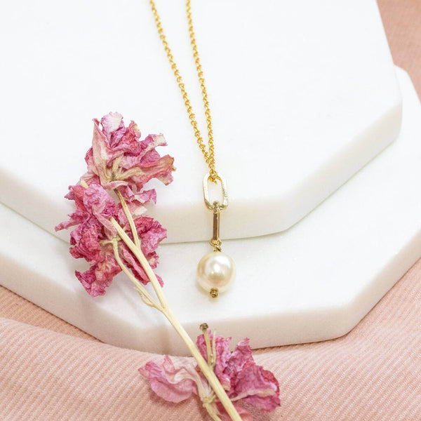 Chunky chain pearl necklace lying on white hexagon coasters with pink dried flower and on pink material