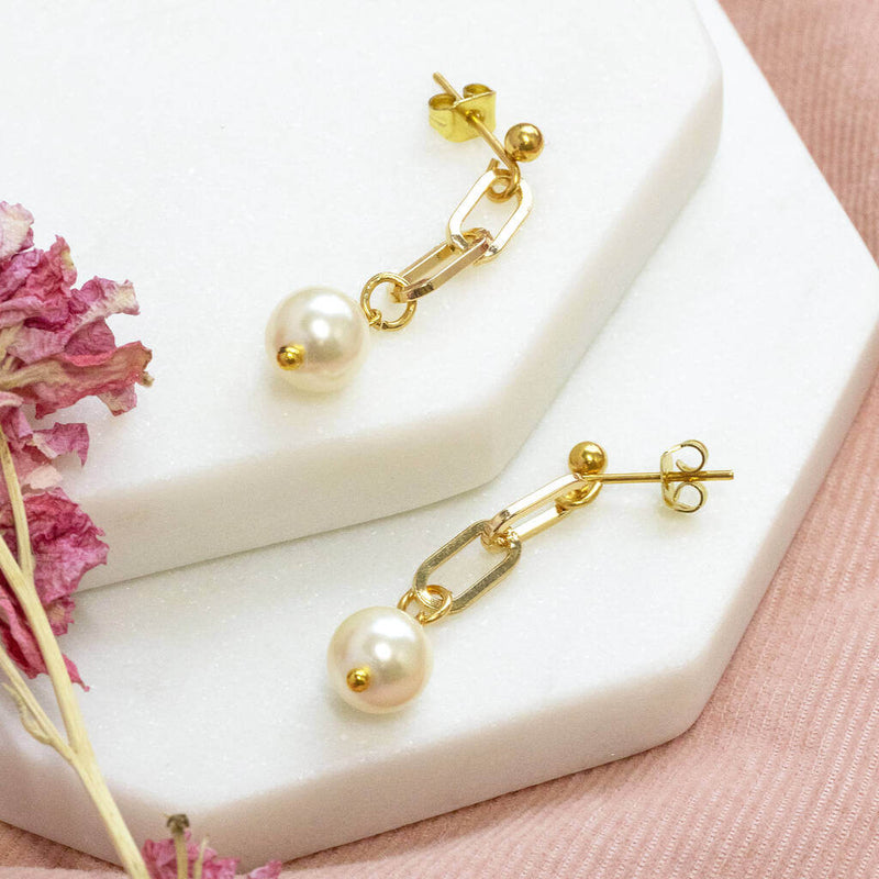Chunky chain pearl earrings lying on white hexagon coasters with pink dried flower and on pink material