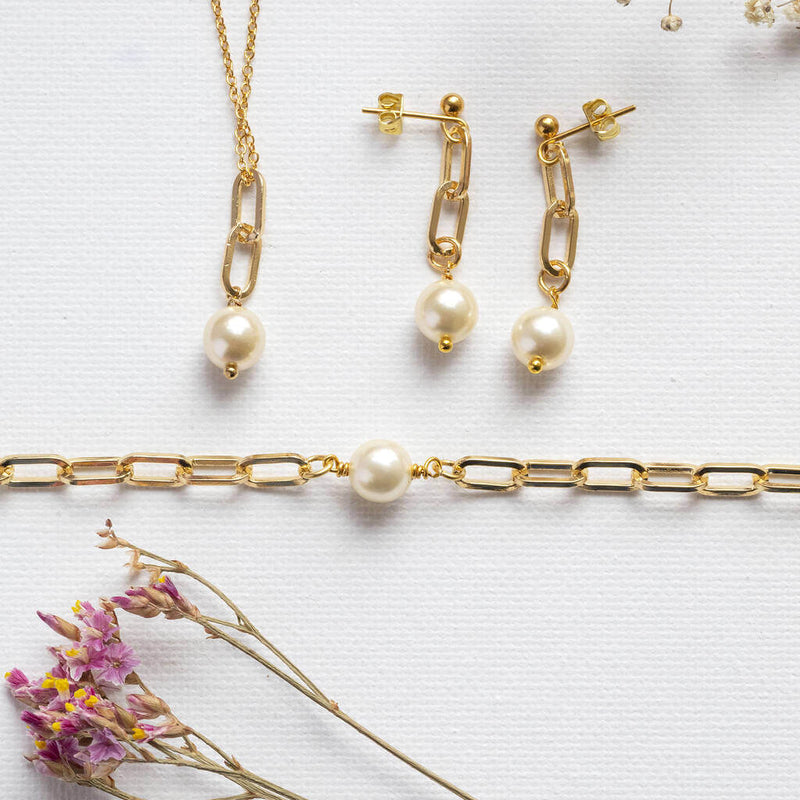 Chunky chain pearl jewellery set lying on white background with pink and yellow dried flower at the bottom