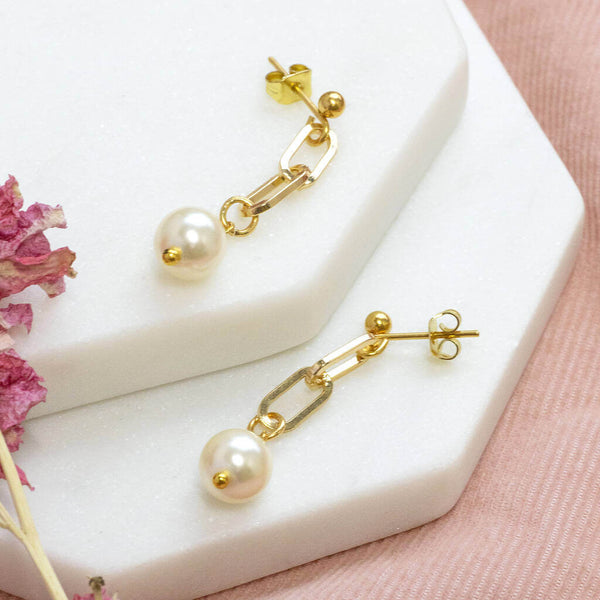 Chunky chain Swarovski pearl drop earring lying on 2 white hexagon coaster with one earring higher
