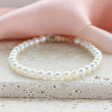 Classic pearl bracelet lying on a stone tile with pink material at the back