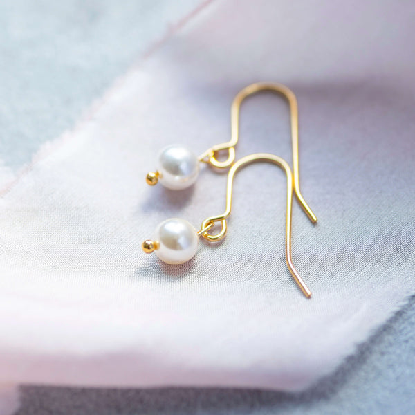 Gold classic pearl drop earrings with classic ivory pearl laying on pink material