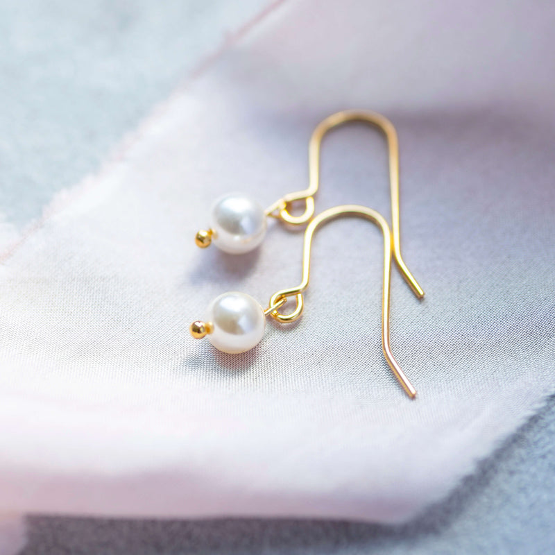 Gold classic pearl drop earrings with classic ivory pearl laying on pink material