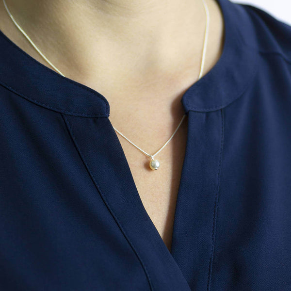Model wears classic pear drop pendant necklace in silver with an ivory pearl with navy top
