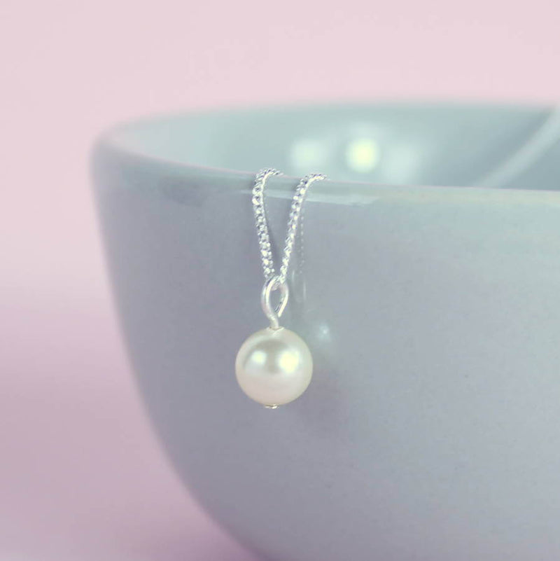 close up of an ivory pearl hanging off a blue bowl with silver chain 