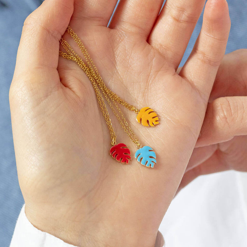 Image shows model holding red, blue and orange Dainty Monstera Leaf Enamel Necklace