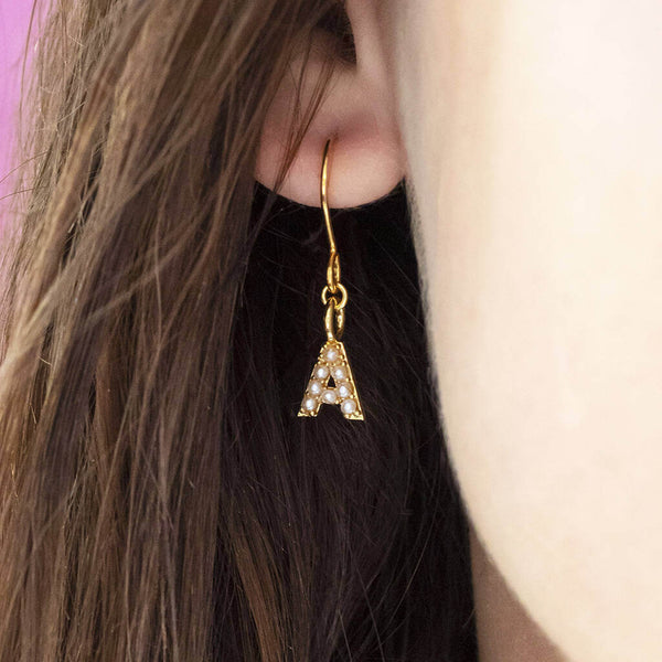 Model wears dainty pearl initial charm earring with the initial A