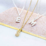 Three dainty pearl initial necklaces, 2 silver with the initial E and M and one gold with the initial S lying on a pink background with gold trim 