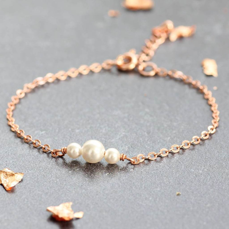 Delicate pearl trio bracelet in rose gold lying on grey counter
