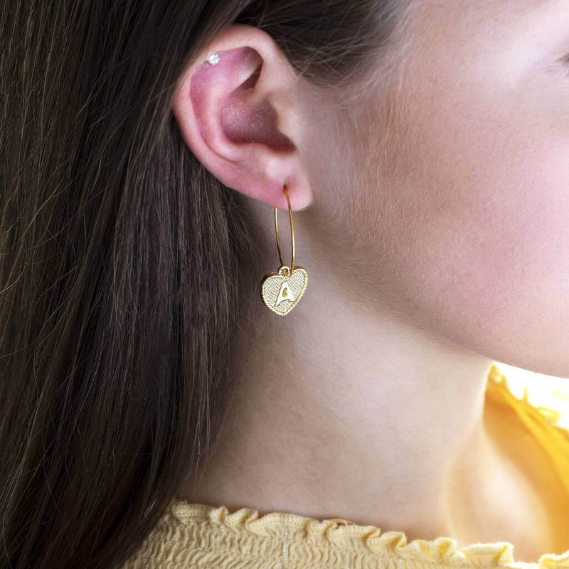 Image shows model wearing gold dotted heart initial hoop earrings with initial A