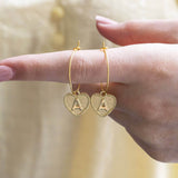 Image shows model holding gold dotted heart initial hoop earrings with initial A