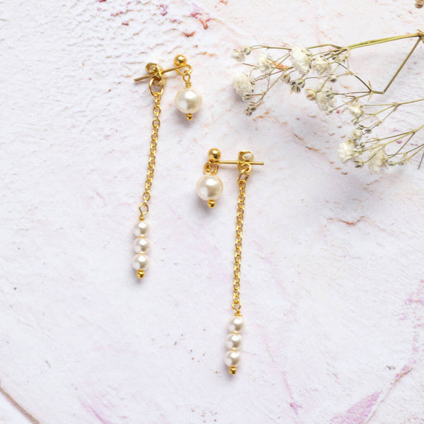 Double drop pearl chain earrings lying pinky white background with white dried flowers at the side