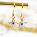 Imgae shows Evil Eye Enamel Star Earrings hanging from a gold rail