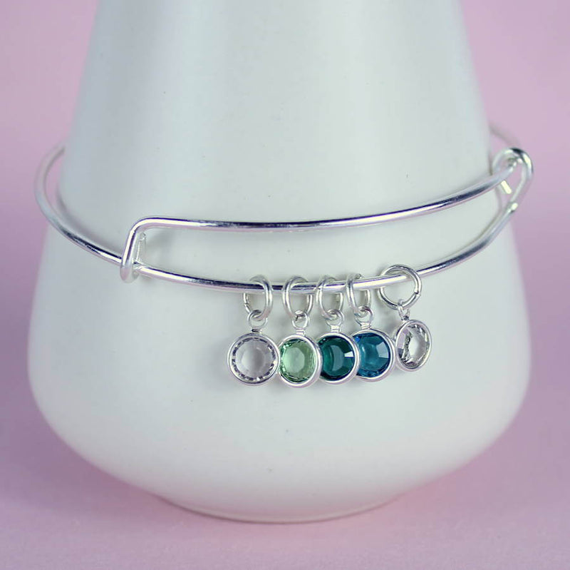 Image shows family birthstone bangle with  light amethyst, peridot, emerald, blue zircon and crystal birthstones