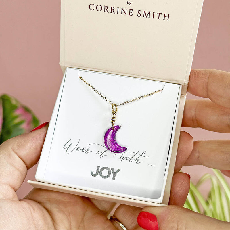 Image shows one of the Four in One Glass Moon Necklaces in a gift box on a wear it with joy sentiment card