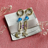 Image shows Frosted Blue Moon and Star Earrings lying on a Joy suedette pouch