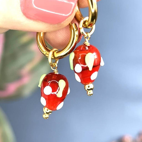 Image shows model holding strawberry charm earrings