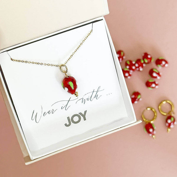 Image shows glass strawberry necklace in a gift box with the wording wear it with joy