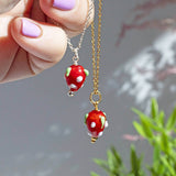 Image shows models hand holding necklaces with strawberry charm detail