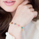 Model wears gold family birthstone link bracelet. Visible birthstones from left to right: February Amethyst, September Sapphire, October Rose, December Blue Zircon.