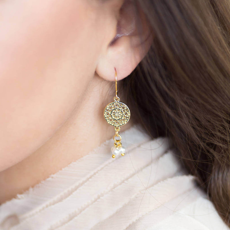 Model wears gold filigree earrings with triple pearl drop