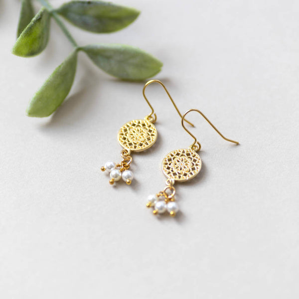 gold filigree earrings with triple pearl drop lying on off white back ground 