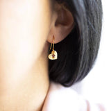 Image shows model wearing gold heart birthstone charm earring with July birthstone