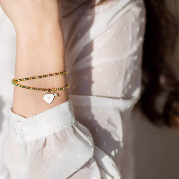 Model wears gold heart and perl charm bracelet 