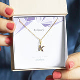 Image shows model holding a gift bow with gold birthstone initial necklace with the initial K February birthstone on a  February  birthstone characteristics card