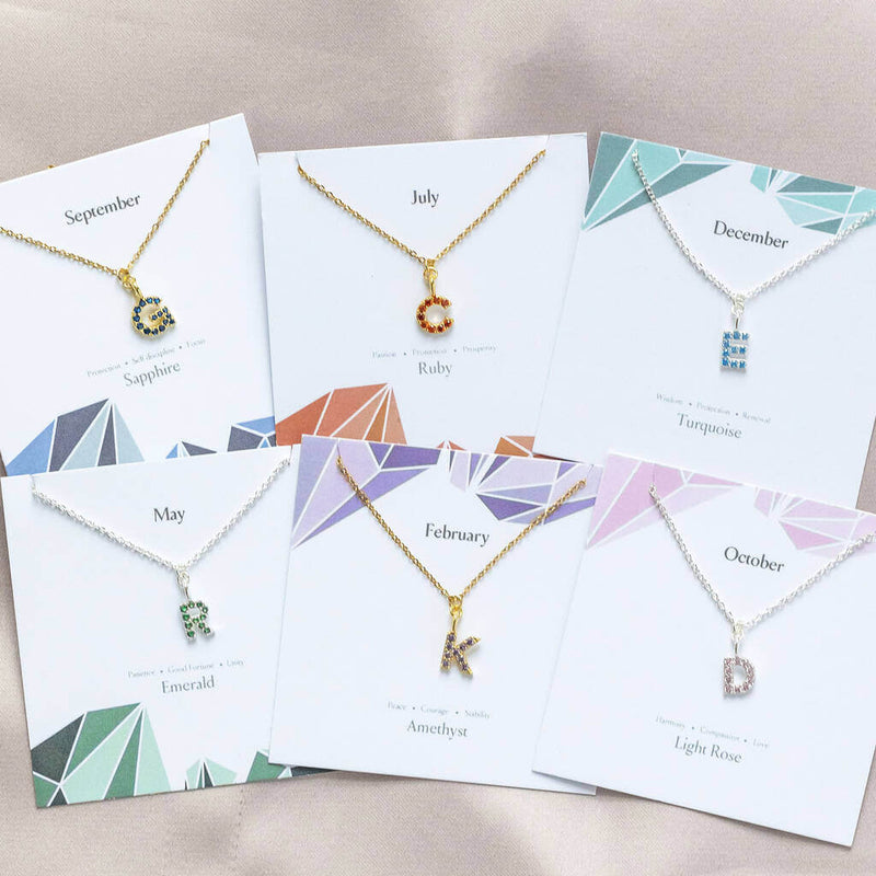 Image shows a selection gold and silver birthstone initial necklace birthday characteristic cards