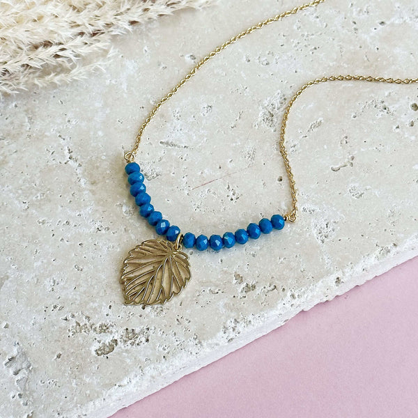 Image shows Gold Plated Leaf Necklace with Indigo Bead Detail lying on a stone slab