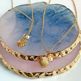 Image shows gold plated shell necklaces displayed on blue and pink trinket dishes