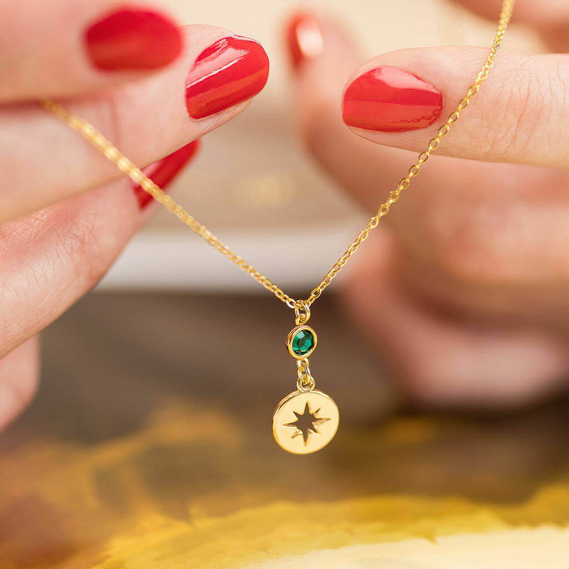 Image shows model holding gold starburst birthstone necklace with May birthstone