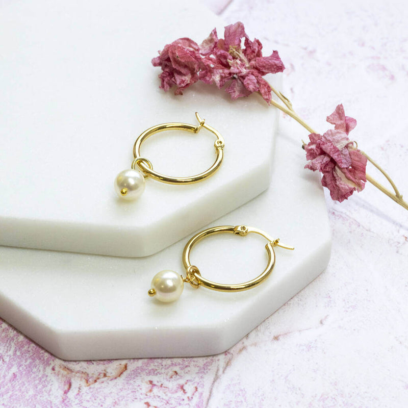 Hinged hoop earrings with Swarovski pearl detail  lying on two stacked with hexagon coasters with dark pink dried flower the side