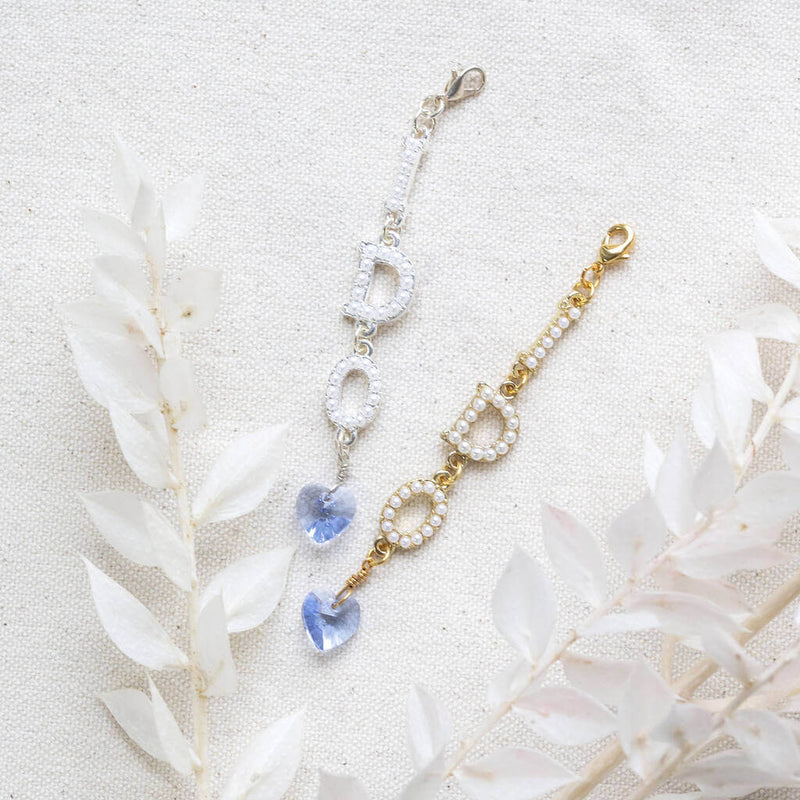 Silver and Gold I do something blue wedding charm lying on cream linen with white dried leaf next to them