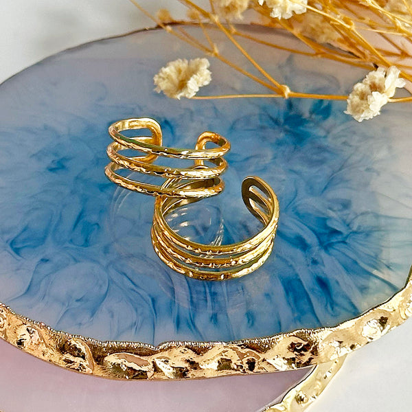 Image show adjustable triple band gold rings on a blue glass background