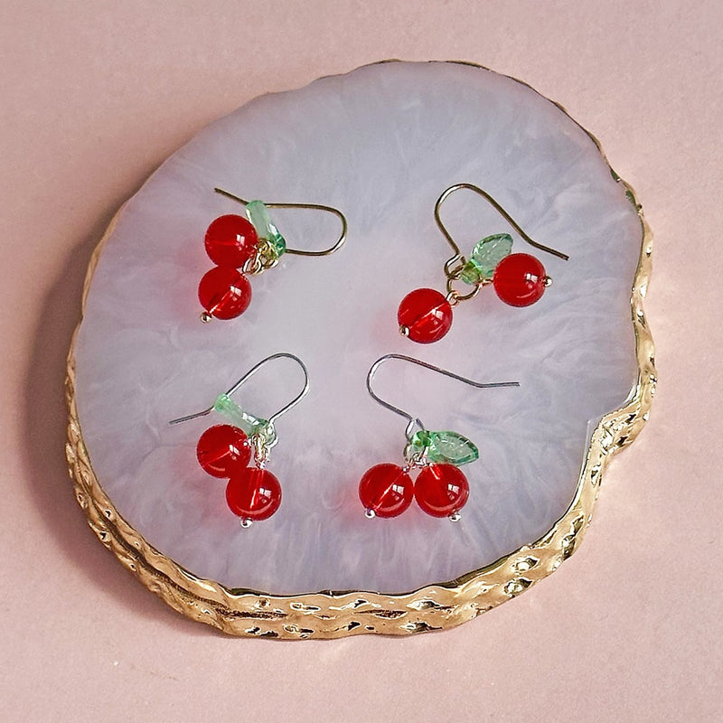 Images shows gold and silver plated glass cherry earrings on a gold edged trinket dish
