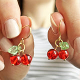 Image shows a hand holding up a pair of handmade gold plated glass cherry earrings