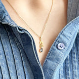 Image shows model in denim shirt wearing a leaf necklace with September sapphire birthstone detail