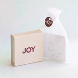 Image shows with a white ribbon and a JOY tag JOY gift box with JOY logo in maroon, and white organza bag with a sentiment card inside, finished