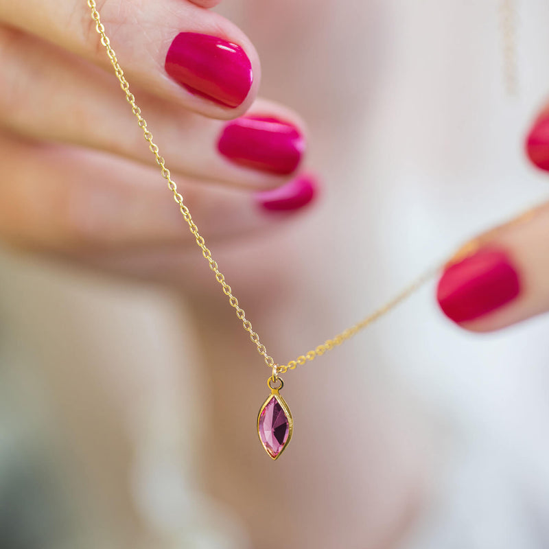 Image shows model holding gold Marquise Swarovski Crystal Birthstone Pendant Necklace with October birthstone