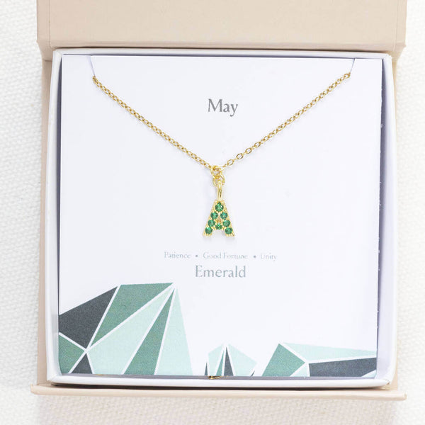 Image shows gold May birthstone emerald initial necklace in a gift box on a May birthstone characteristics card