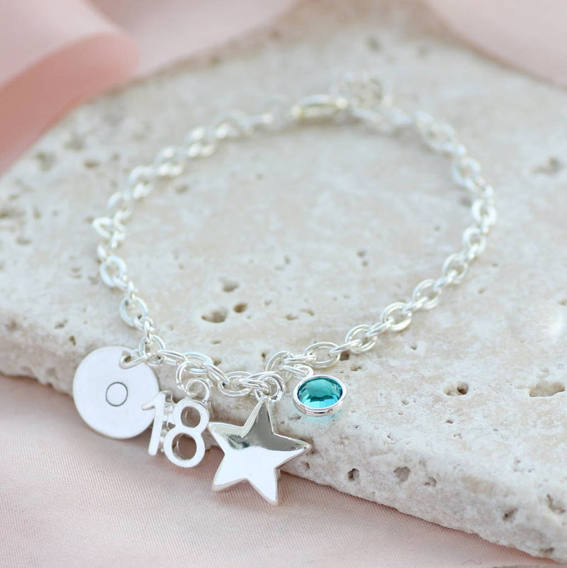 Image shows milestone birthday personalised charm bracelet with initial disc O, number 18, star charm and Blue zircon birthstone
