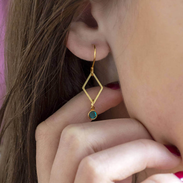 Image shows model wearing minimalist gold rhombus birthstone earring with December birthstone
