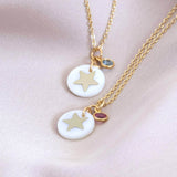 two mother of pearl star necklaces one with March (aquamarine) and the other with October (Rose)l lying on pink material