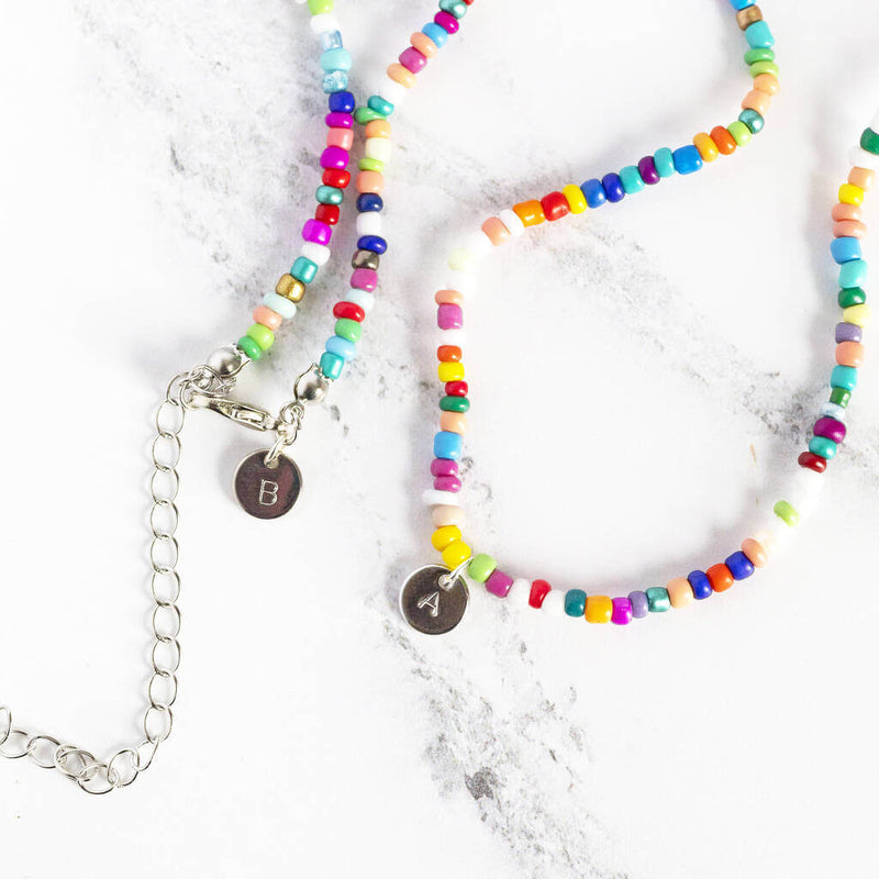 Image shows two multi coloured beaded necklaces showing initial disc at the clasp
