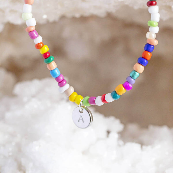 Image shows multi coloured beaded necklace with silver dis with an A on it