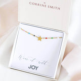 Image shows multicoloured beaded star anklet on a 'wear it with JOY' sentiment card within a JOY by Corrine Smith gift box.