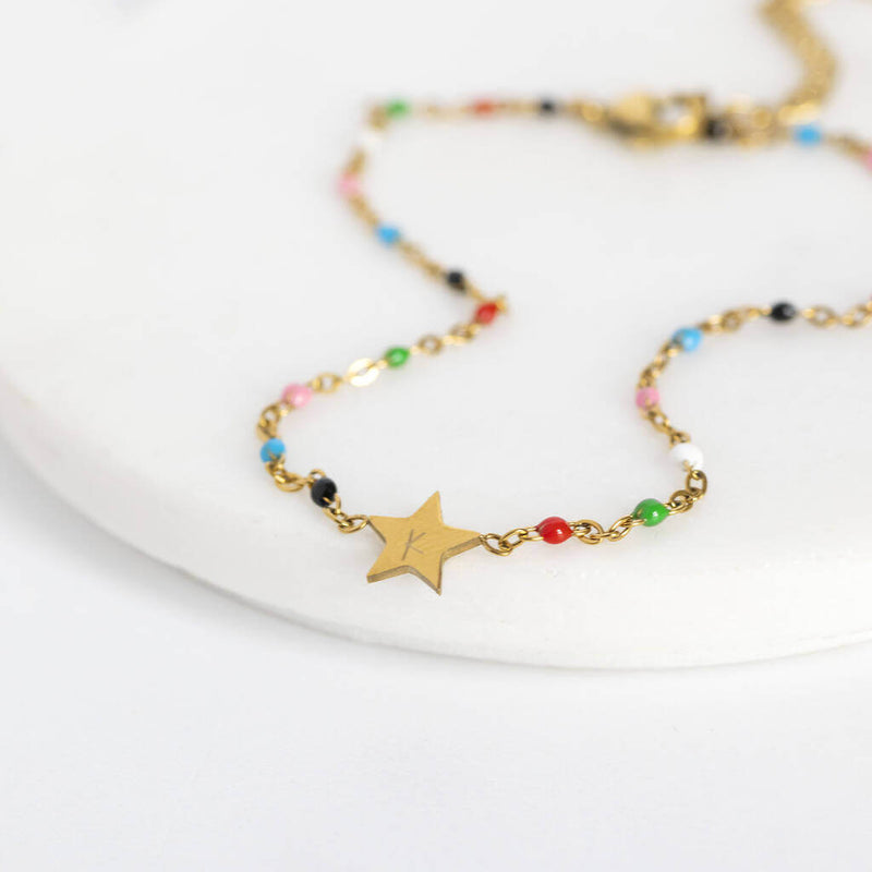 Image shows multicoloured beaded star anklet with a 'K' engraved on the star. Anklet sits on a white backdrop.