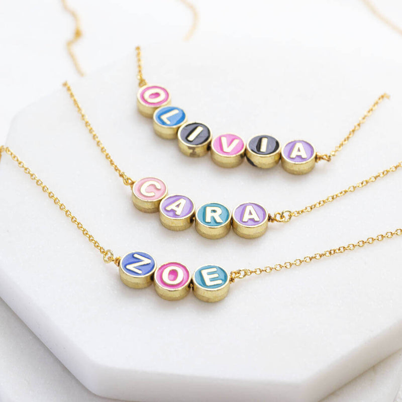 Image shows personalised enamel disc name necklaces with the names Olivia, Cara and Zoe